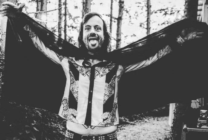 A cheerful man outdoors spreading a cape-like cloth behind him, smiling and sticking out his tongue.