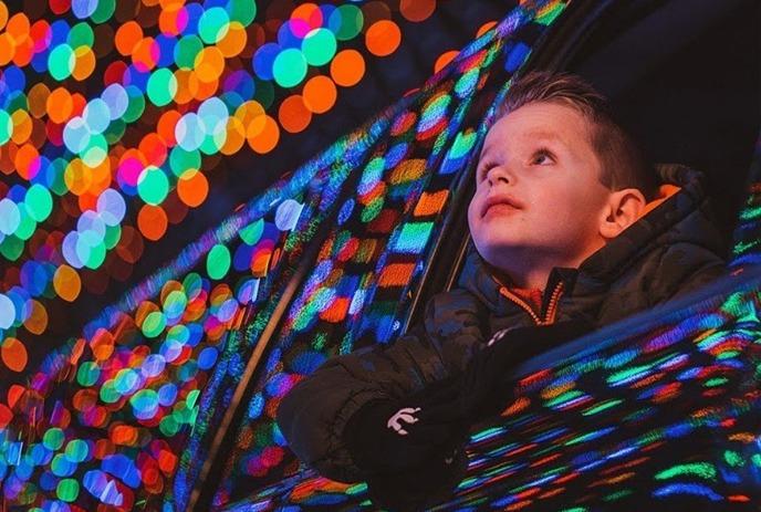 A child in a car with its window open looking at various coloured lights from the Magic of Lights holiday light experience