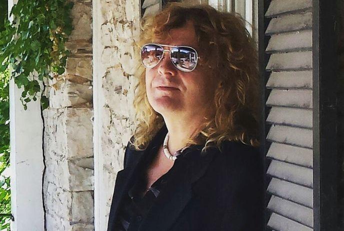 Carl Dixon wearing sunglasses, leaning against a wall outside on a sunny day.