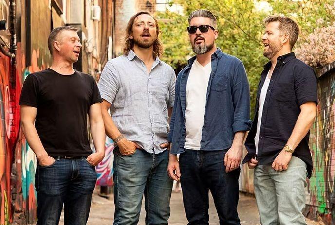 Four members of the band Pressgang Mutiny posing casually in a graffiti-lined urban alley.