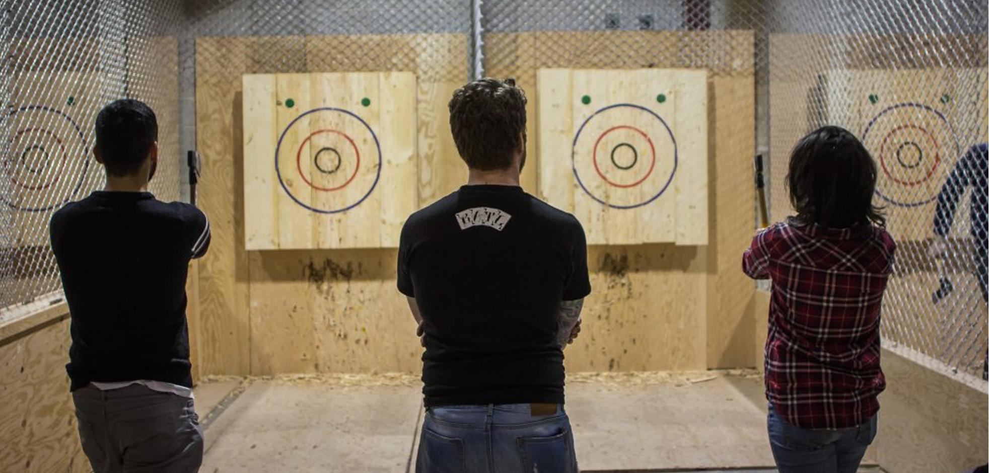 Two people aiming their axes at the target, while another person looks on.