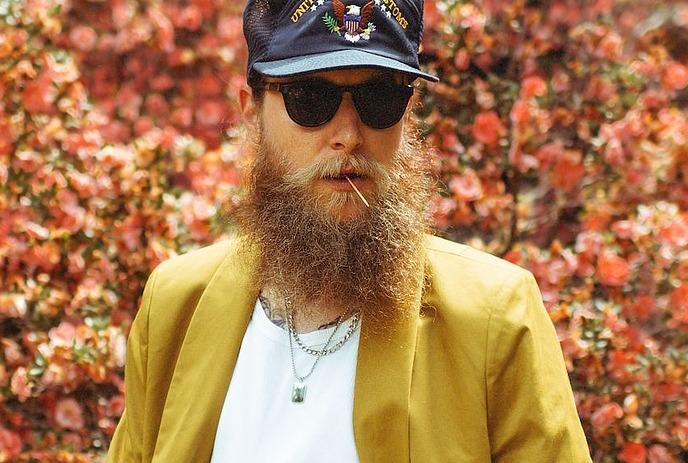 Bearded figure in ornate robes framed by columns, birds, cats, and banner; mythic, temple-like illustration.