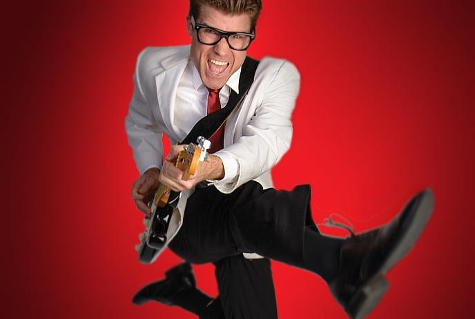Person wearing a white sport coat, playing guitar and dancing.