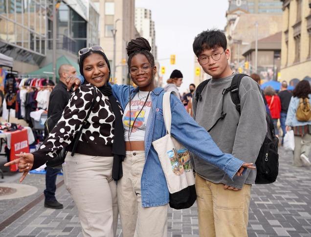 Three friends pose at an outdoor vintage market on Dundas Place.