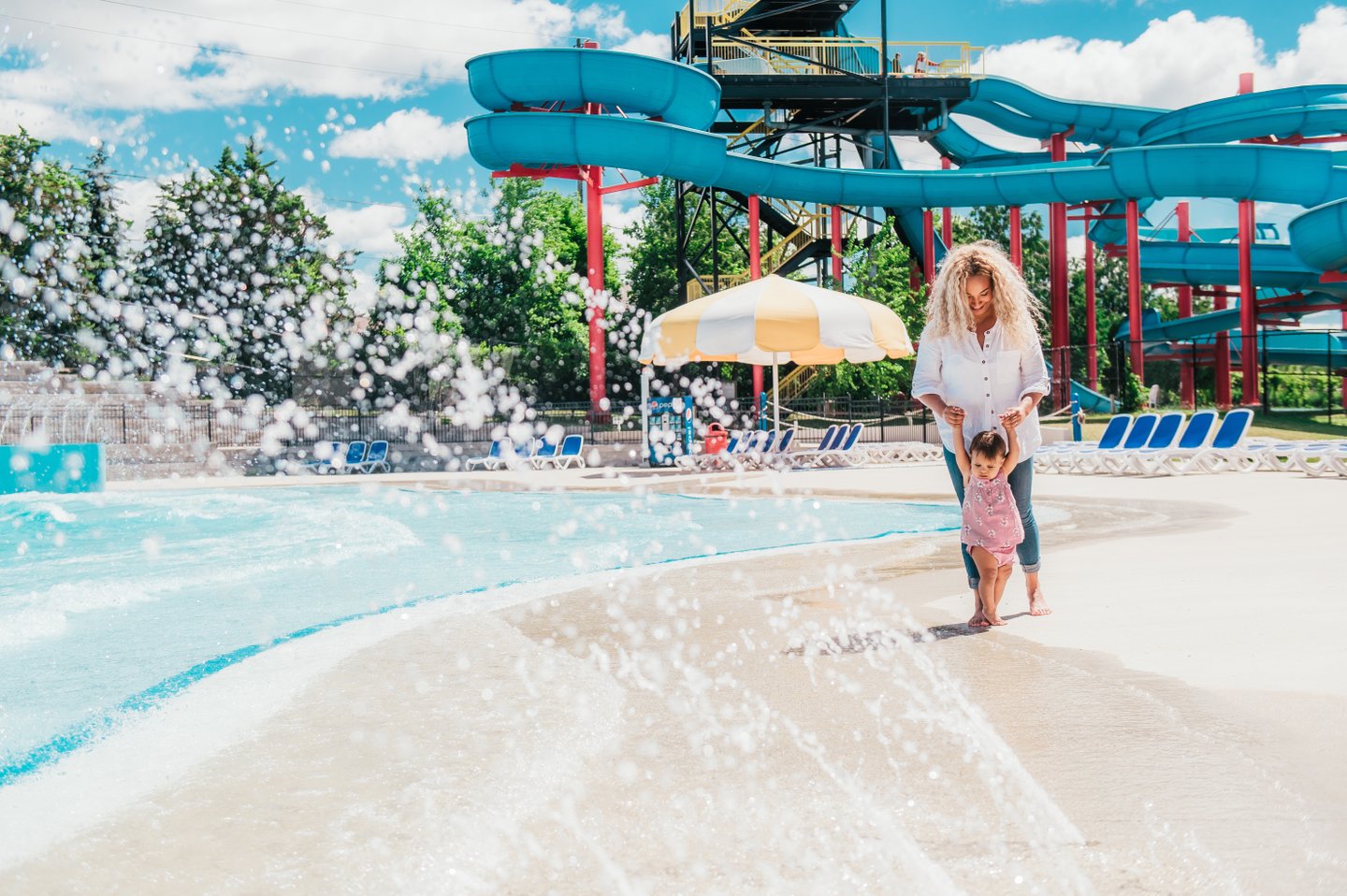 Mother helps child walk through a water jet at East Park waterpark.