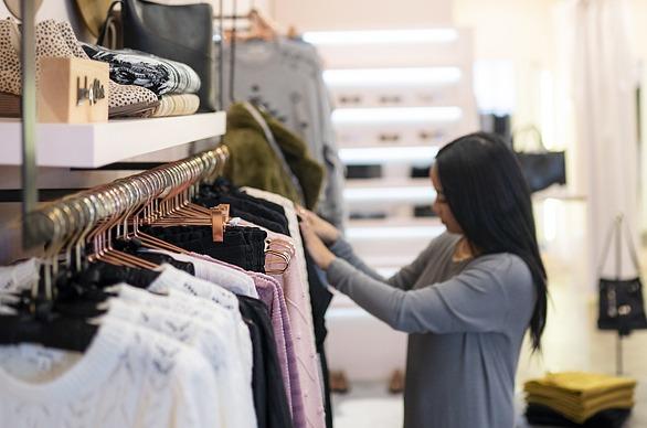 A person looking through various shirts on a rack on display at the store Needs/Wants located in London, Ontario