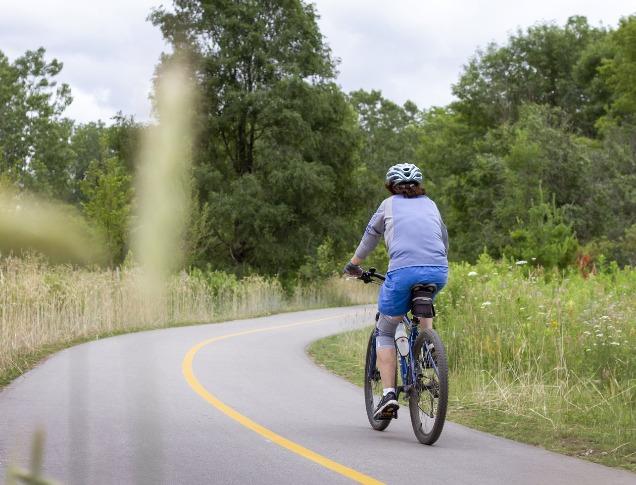 A cyclist bikes along a paved path on the Thames Valley Parkway in London, Ontario.