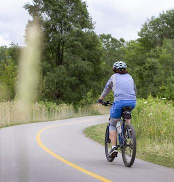 A cyclist bikes along a paved path on the Thames Valley Parkway in London, Ontario.
