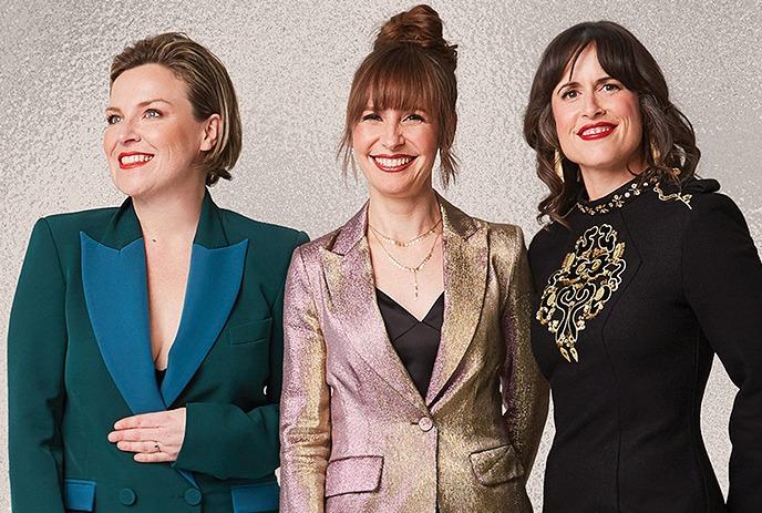 Three members of the band The Good Lovelies smiling and posing in elegant, shimmering outfits.