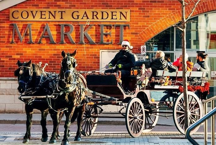 Horse-drawn carriage with passengers in front of Covent Garden Market’s brick building, blending tradition and urban charm.