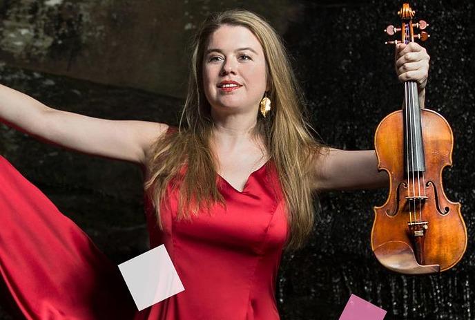 Woman artist in red dress holds violin and bow, standing confidently against a dark, textured background.
