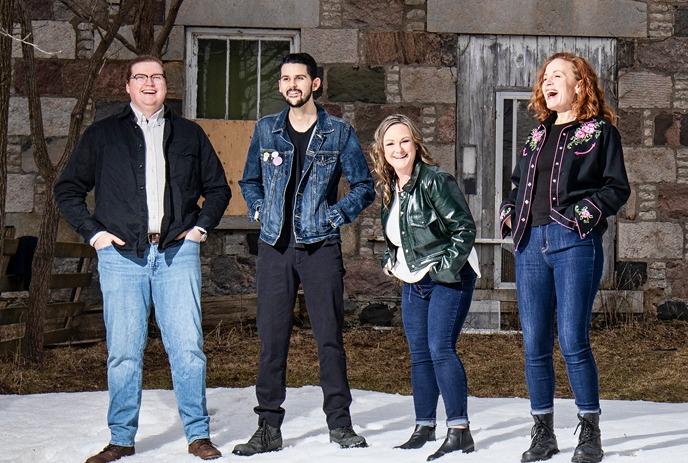 A photo of the band Maggie's Wake, featuring four members standing in front of a stone building with snow on the ground.