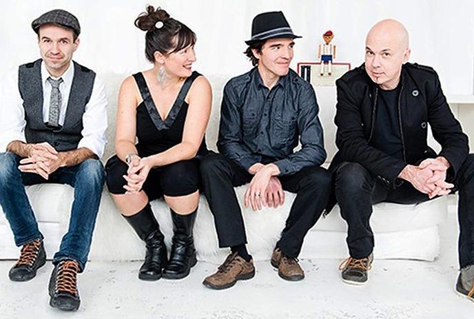 The four band members of Melisande sitting on a white couch in a white room, posing for the camera.