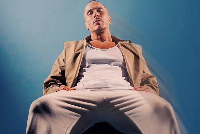 Shawn Desman sitting in a chair looking at the camera, in a completely blue room.