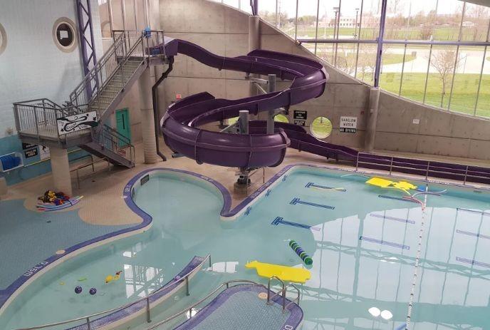 Indoor pool scene with purple slide, toy floats, staircase to slide, bright windows, and play-friendly layout.