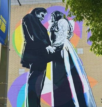 Two figures hold hands in front of vivid shapes: a mural of connection signed by Kevin Ledo on a building wall.