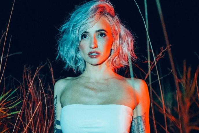 Lights with blue hair and tattoos in a strapless top, lit by red and green lights.