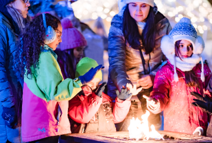People dressed in winter wear, warming themselves by the fire.