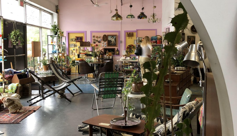 A vintage shop filled with many items, including lamps, chairs, plants and kitchen decor.
