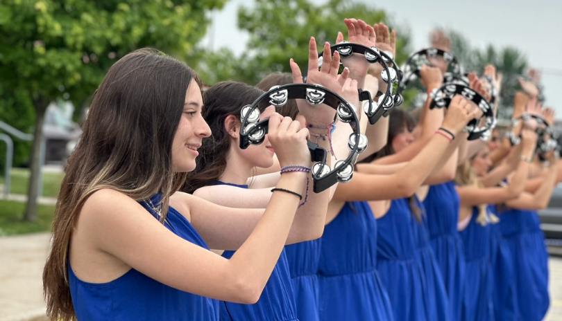 A line of dancers dressed in blue with tambourines in the air.