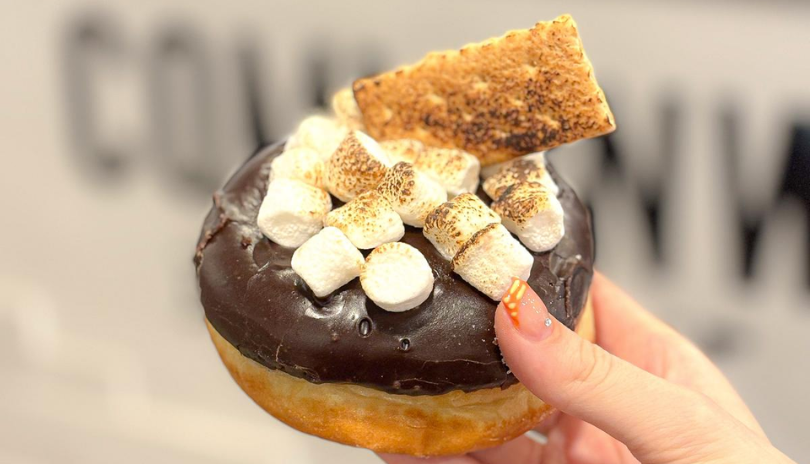 A hand holds a smore's flavoured donut with marshmellows and graham cracker on top.