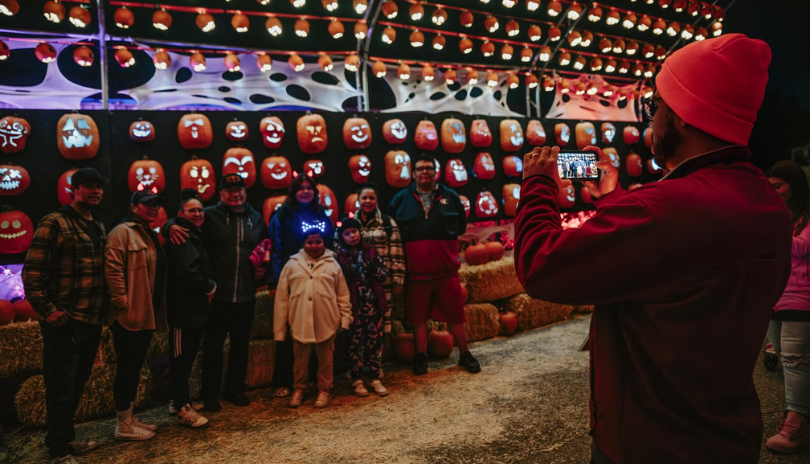A person takes a photo of a family in front of a wall of carved pumpkins.