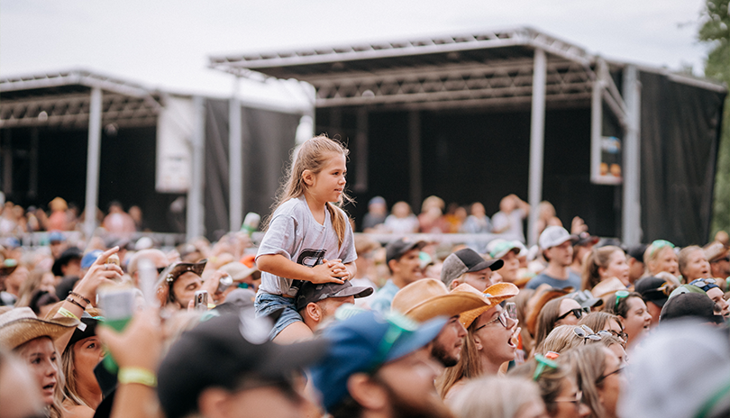 Child sitting on an adults shoulders enjoying an outdoor concert
