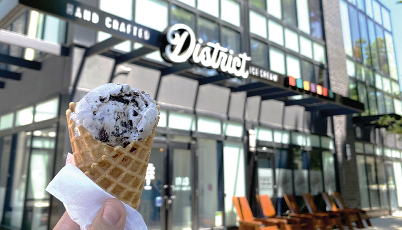 Ice cream cone being held up outside in front of The District ice Cream shop