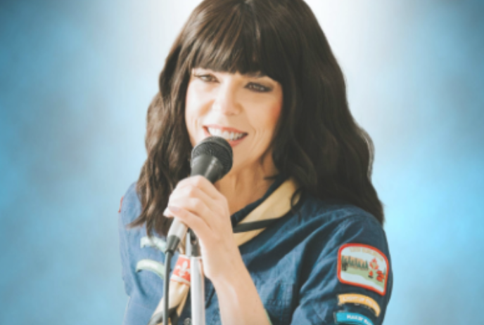 Person holding a microphone and a tambourine, smiling.