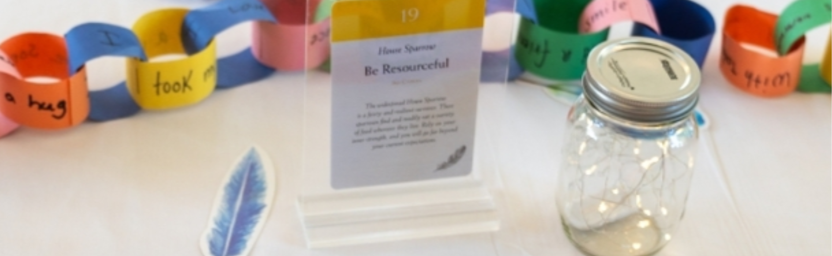 Colourful paper chain with a feather and a jar inside it.